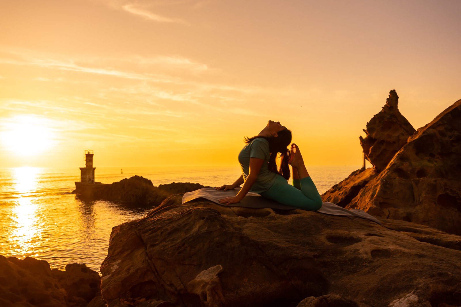 Anjaneyasana, A woman doing meditation and yoga exercises at sunset next to a lighthouse in the sea, healthy and naturist life, outdoor pilates